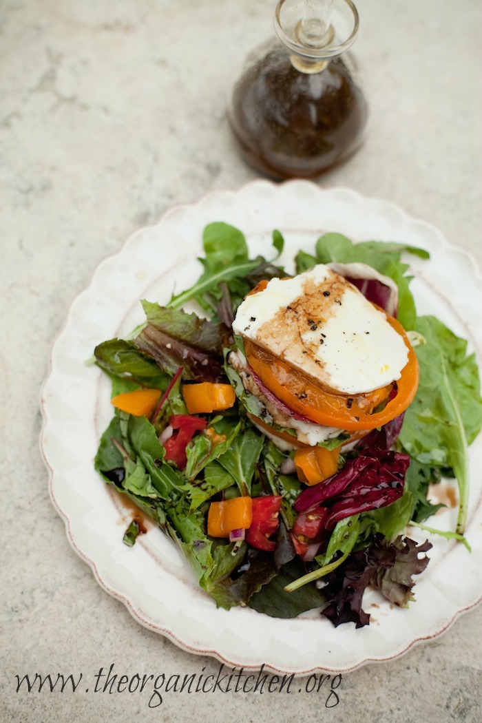 The Caprese Stack Salad on white plate with bottle of balsamic vinaigrette