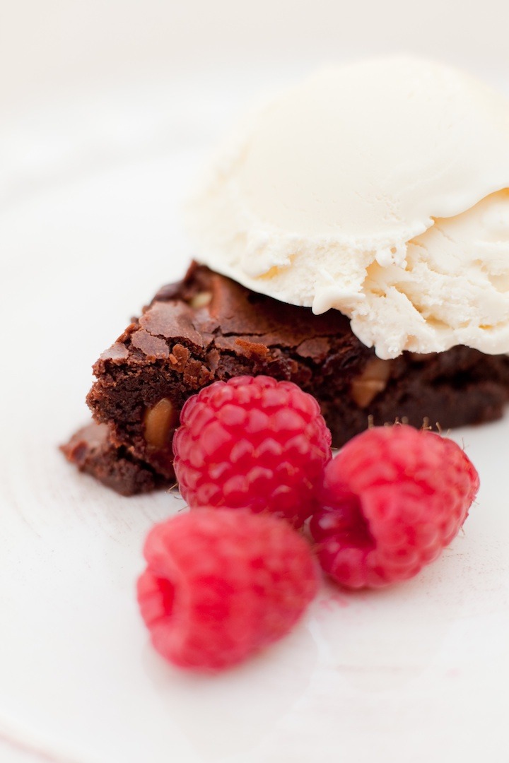 A close of of brown butter brownies with macadamia nuts with ice cream and berries