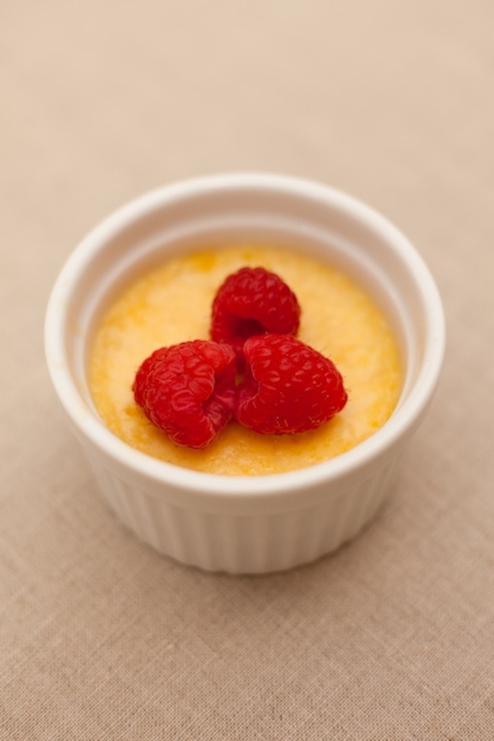 Orange Vanilla Creme Brulee in a white ramekin topped with fresh raspberries