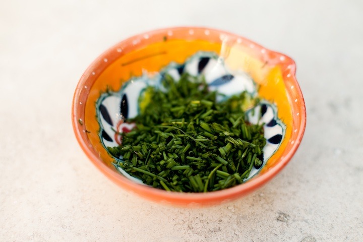 A brightly colored bowl with freshly chopped chives to be used in Decadent Smashed Potatoes