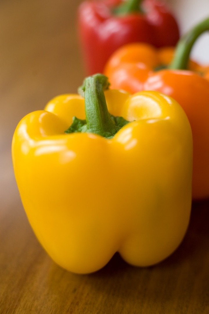 A yellow, orange and red bell pepper on a wood surface
