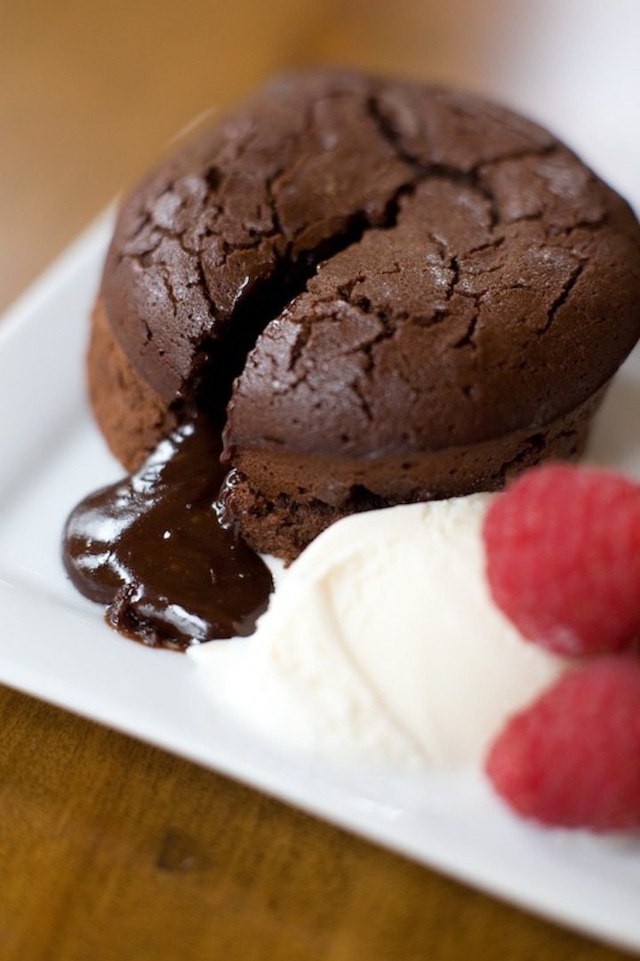 Molten Spiced Chocolate Pomegranate Cakes Molten Spiced Chocolate Pomegranate Cakes on a white dish with ice cream and raspberries on the side