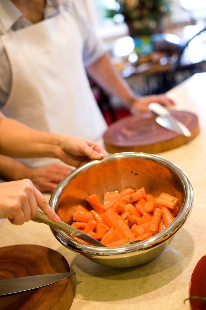 A silver mixing bowl with chopped carrots and herbs in preparation for making Roasted Carrots and Gremolata