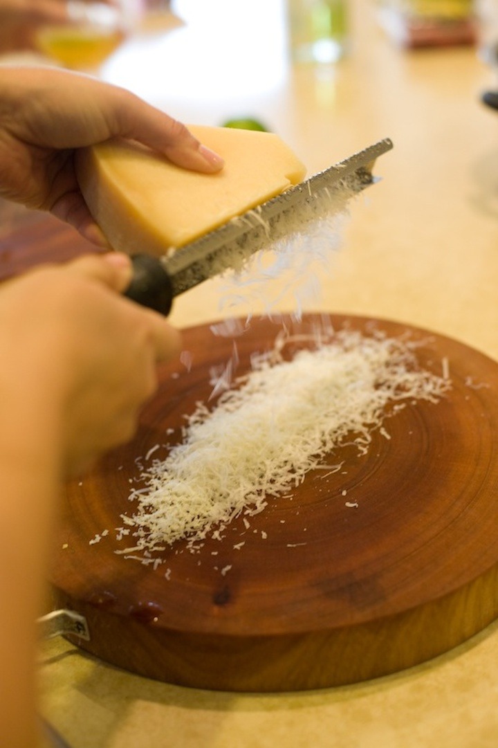 Female hands grating Parmesan cheese onto a cutting board to be used in Decadent Smashed Potatoes