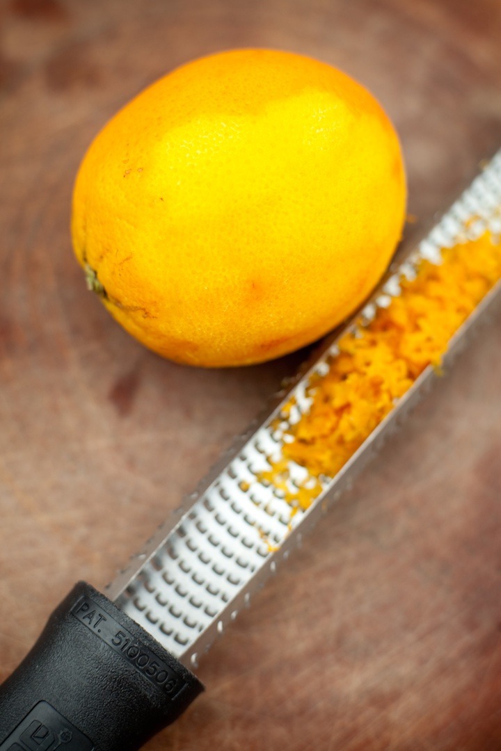 An orange with a microplane full of orange zest on a cutting board