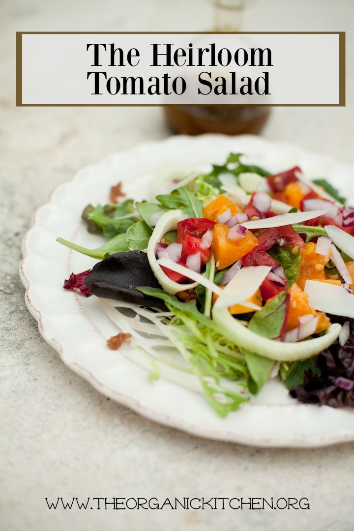 The Heirloom Tomato Salad on a white plate with a bottle of balsamic vinaigrette in the background