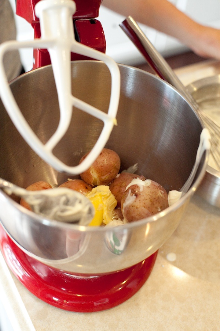 A stand mixer with new red potatoes and butter in the bowl to be used in Decadent Smashed Potatoes