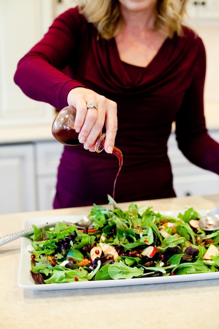 A blonde woman dressing a platter of Greens with Pomegranate Vinaigrette