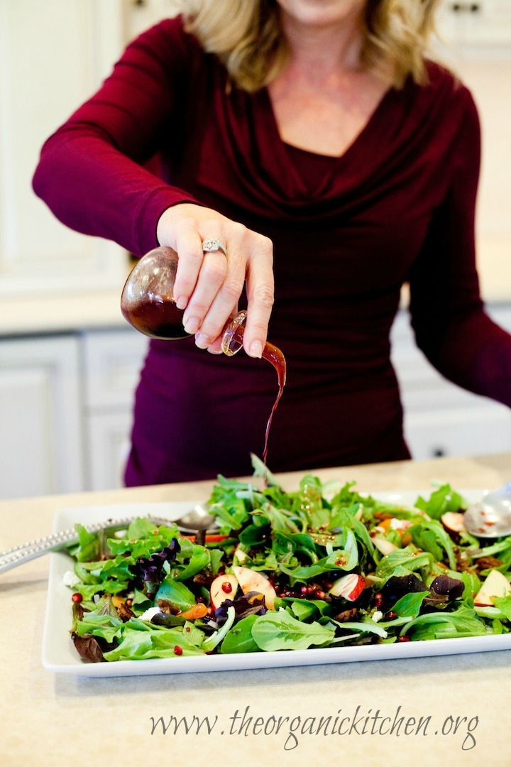 My Favorite Winter Salad Dressings: a woman pouring pomegranate vinaigrette onto a salad