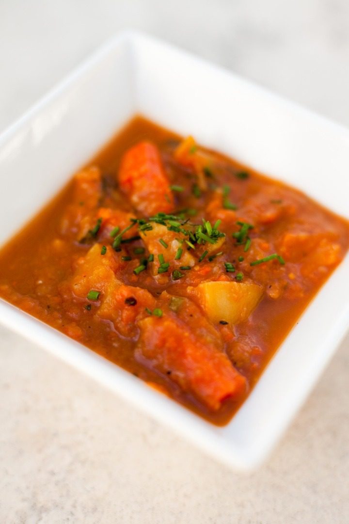 A close up shot of a square white bowl filled with roasted vegetable soup garnished with chives