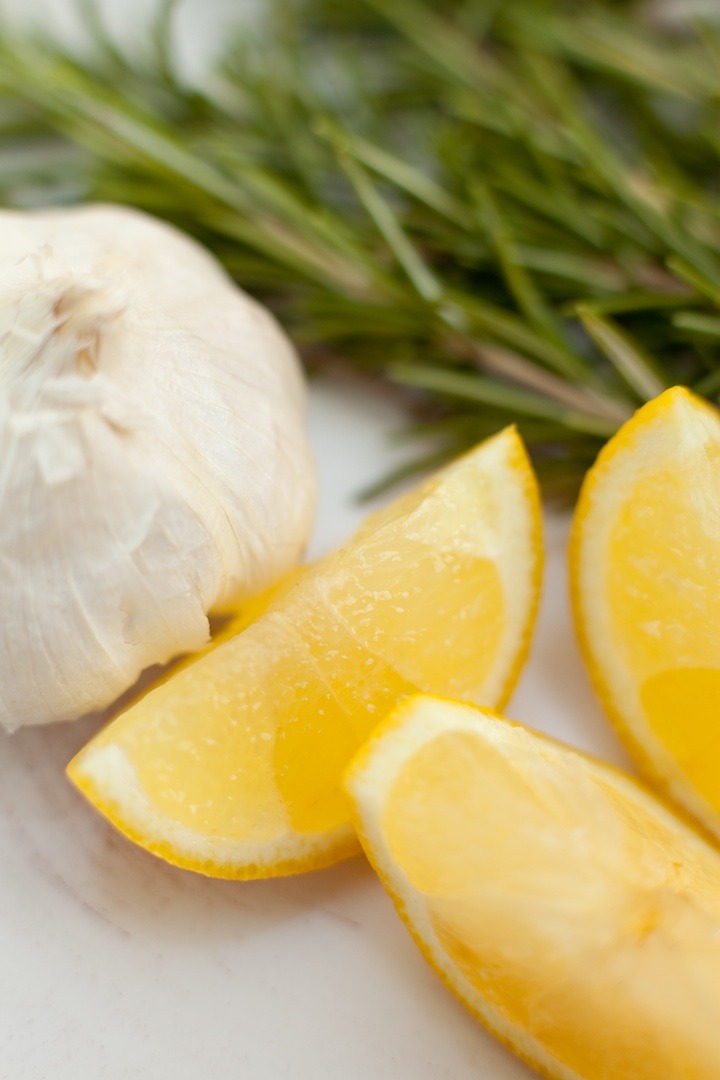 A head of garlic, lemon slices and rosemary springs to be used in recipe for Roasted Lemon Garlic Chicken
