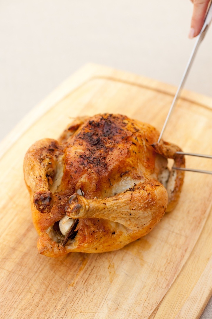 A females hadns holding carving utensils to show how to carve Roasted Lemon/Garlic Chicken with Shallots