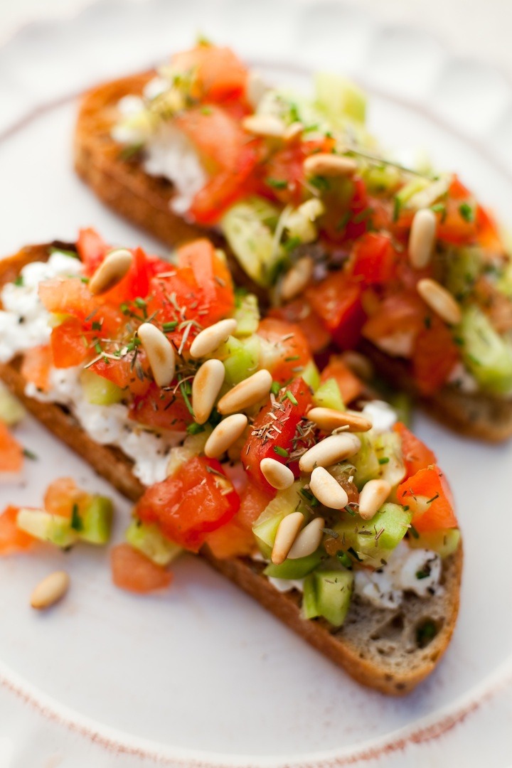 Two slices of toast topped with tomatoes, cucumbers and cottage cheese on white plate
