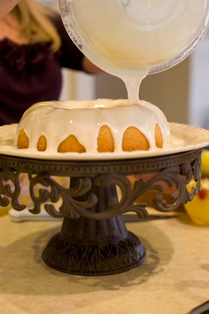 A woman pouring glaze over Orange Cranberry Pound Cake on a fancy cake plate