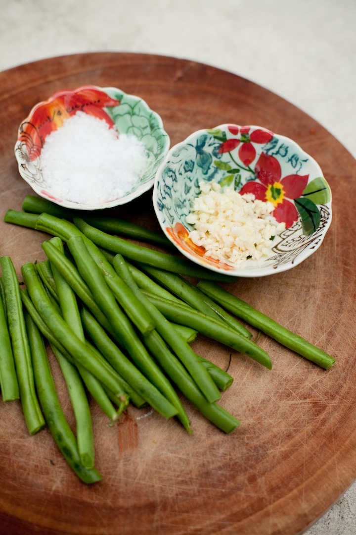 Ingredients for simple blanched green beans: sea salt, garlic and green beans, on a wooden cutting board