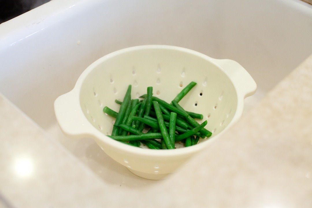 Simple blanched green beans in a colander set in a sink