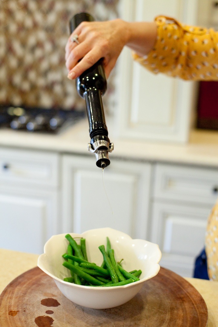 A woman's hand holding a bottle of olive oil to drizzle on simple blanched green beans