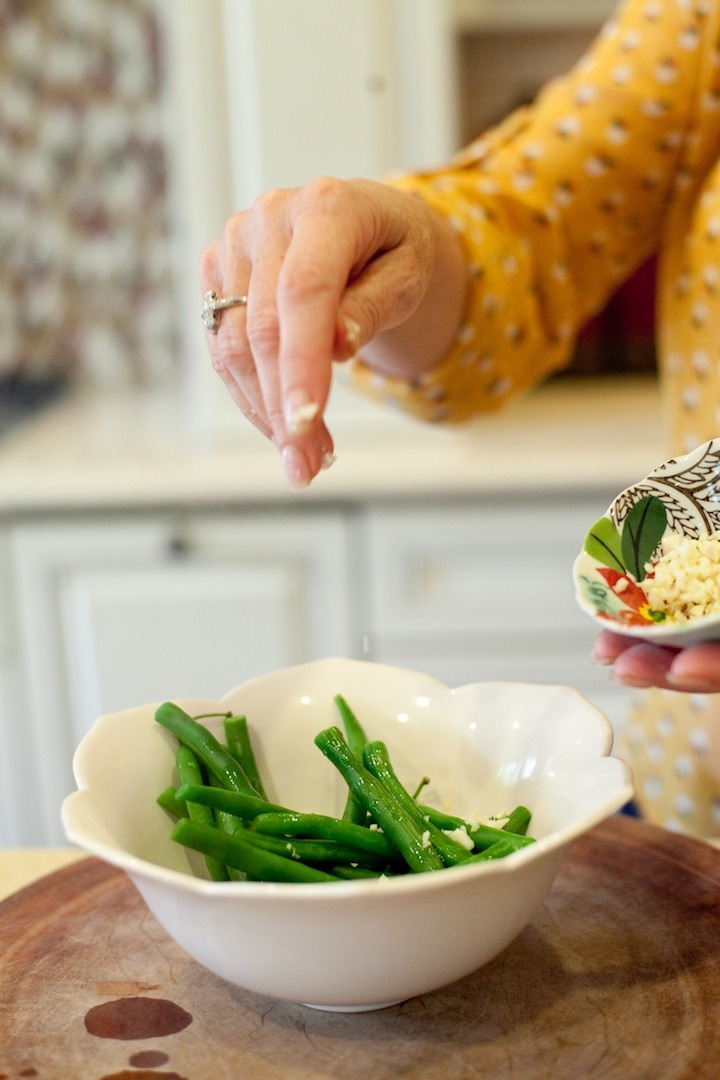 A woman's hand sprinkling minced garlic on a bowl of simple blanched green beans