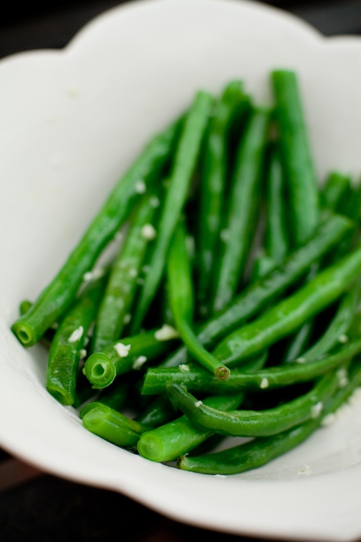 A close up photo of simple blanched green beans in a white bowl on black background