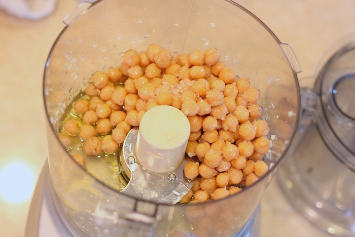 A food processor filled with garlic, garbanzo beans. sea salt and lemon juice
