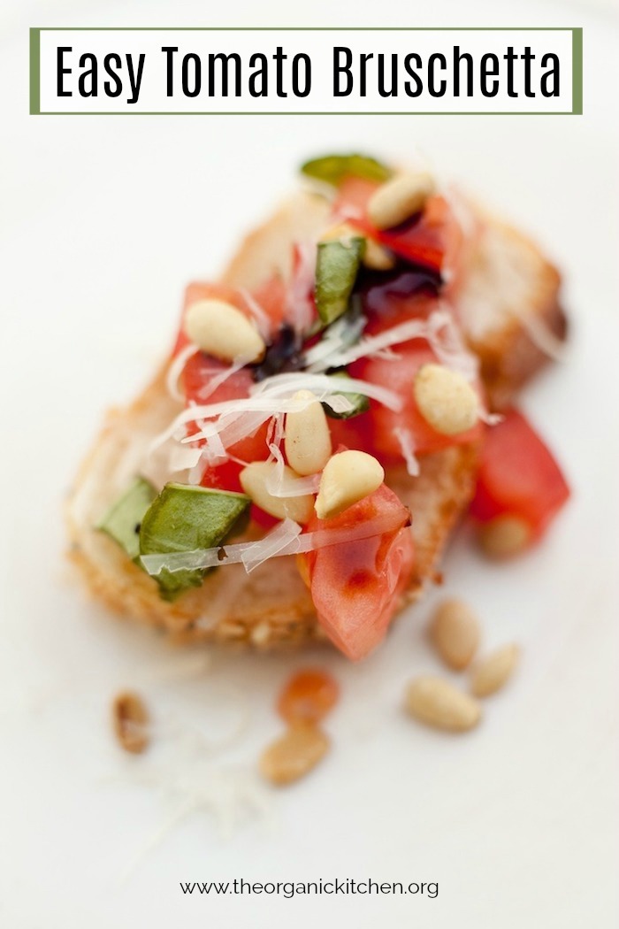A slice of Easy Tomato Bruschetta garnished with parmesan, pine nuts, and basil on white plate