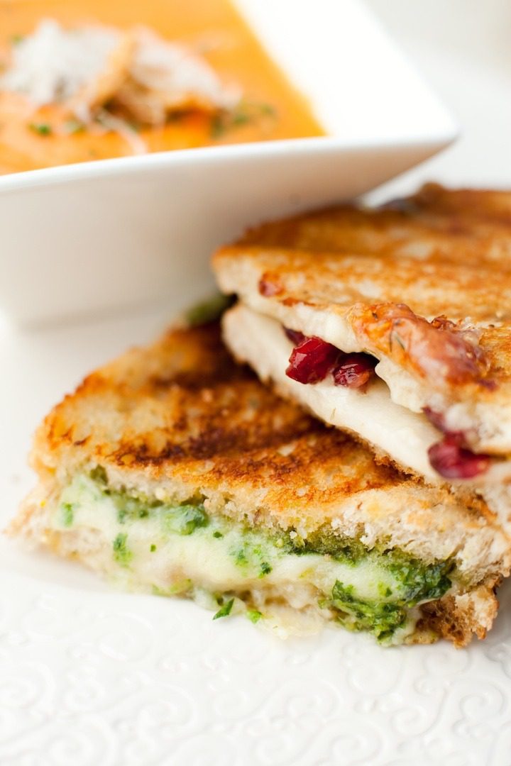 Gourmet Grilled Cheese Two grilled cheese sandwiches on a white plate with a bowl of tomato soup in the background