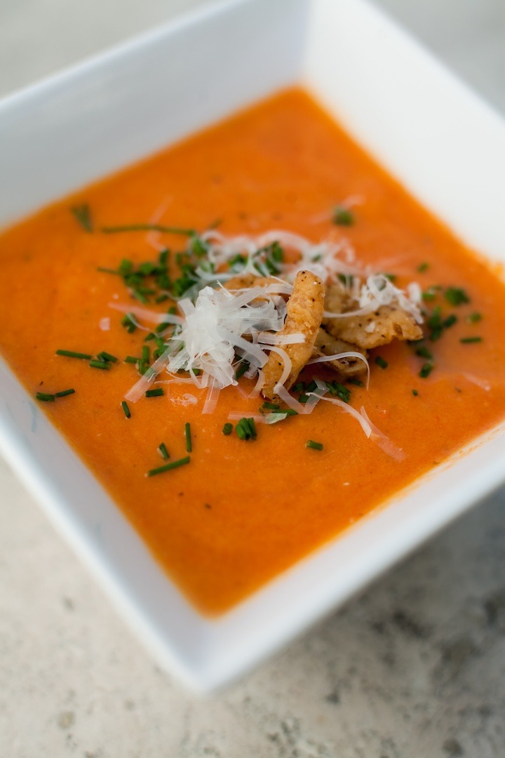 Creamy tomato soup garnished with chives and parmesan in a white bowl 