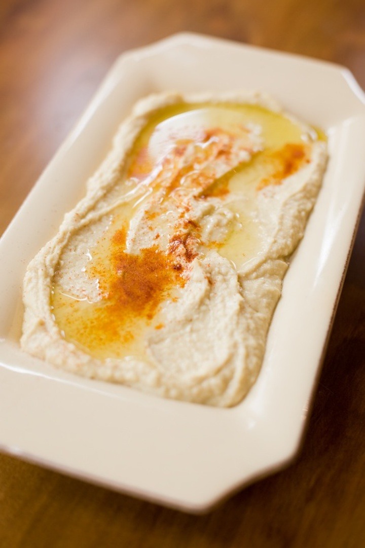 A beige dish filled with hummus topped with olive oil and paprika