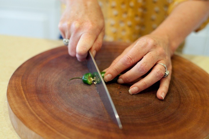 How to Handle a Hot Chili Pepper: a woman using a knife to cut off the root end of a chili pepper