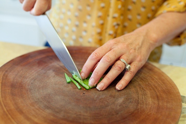 How to Handle a Hot Chili Pepper: a woman's hands slicing a serrano chili with a knife on a cutting board