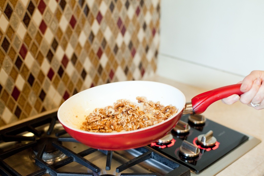 A female lifting a pan filled with nuts to demonstrate How to Caramelize Nuts