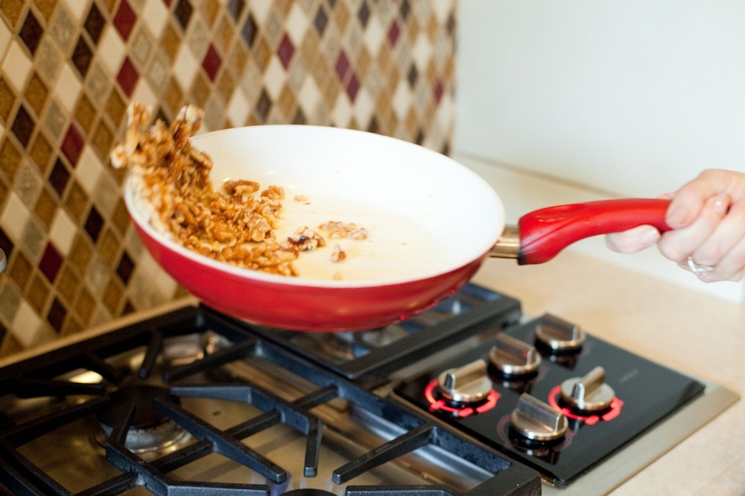 A woman's hand holding a pan and flipping nuts in the air to demonstrate How To Caramelize Nuts