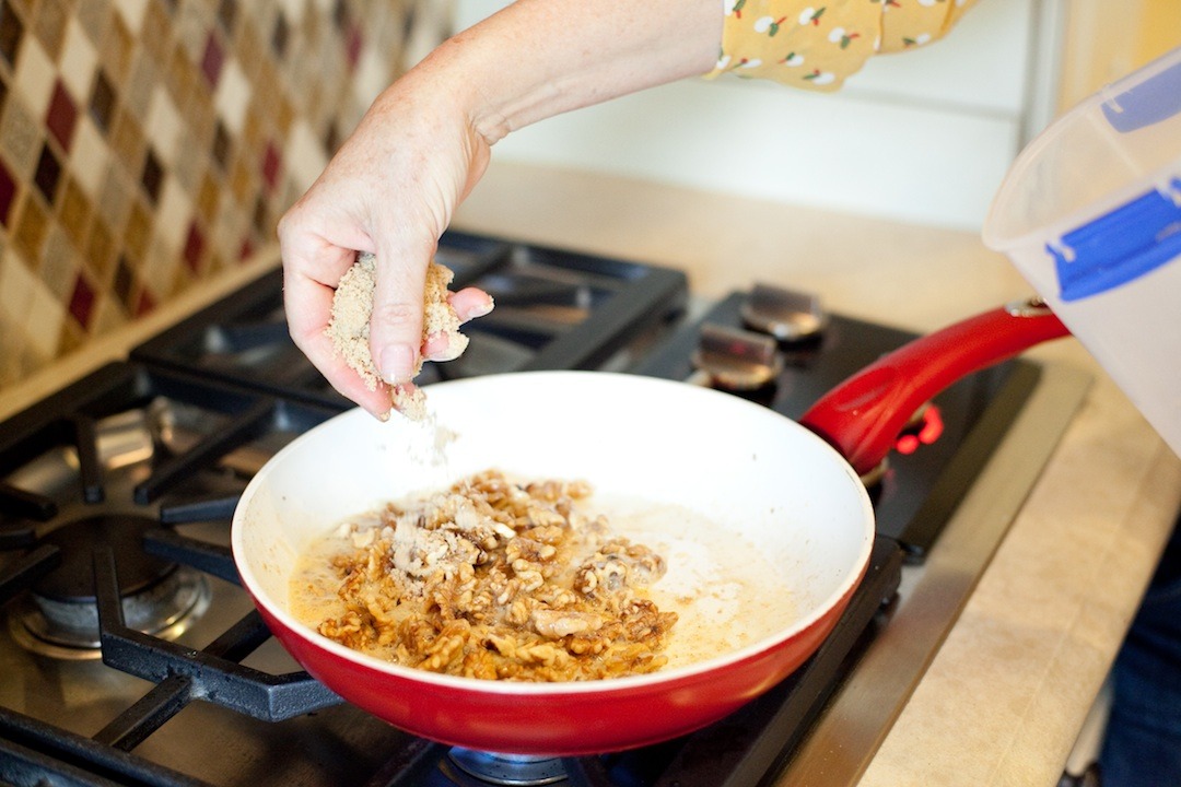 A woman's hand sprinkling brown sugar onto nuts a pan to demonstrate How To Caramelize Nuts