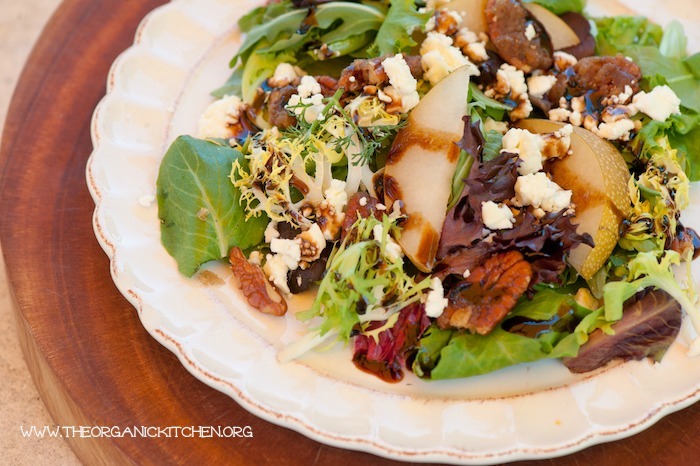 "Greens with Asian Pears and Fig/Maple Balsamic Vinaigrette" served on a \white plate set on a wooden cutting board