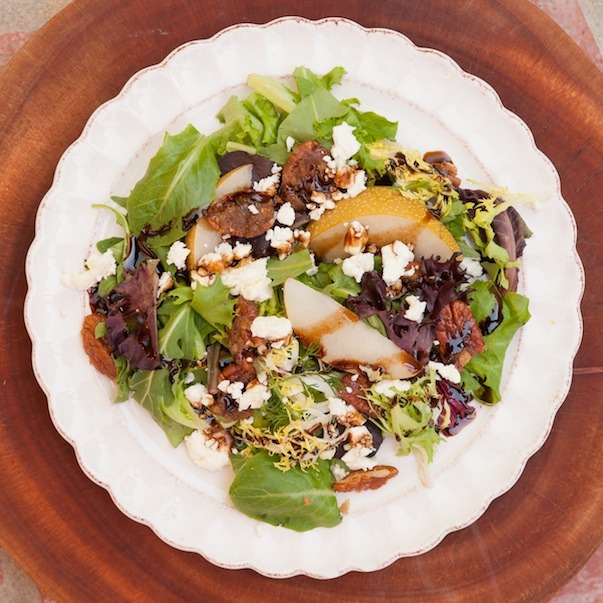 Greens with Asian Pears and Fig Balsamic on a white plate set on a wood cutting board