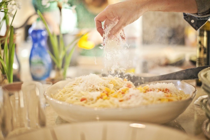 A female hand sprinkling grated parmesan onto a big bowl of Linguini with Sweet Bell Peppers and Serrano Chili
