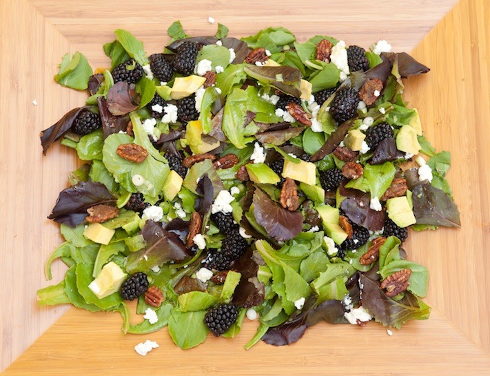 A platter filled with baby lettuce, blackberries, feta cheese , avocado and caramelized nuts