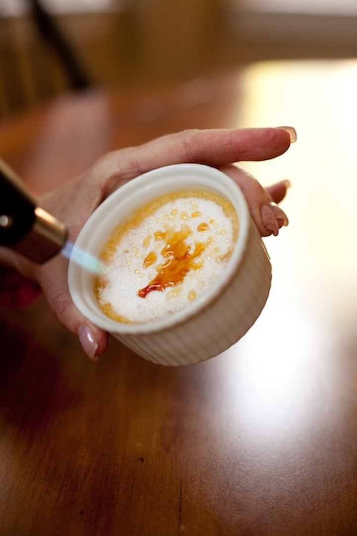 A female's hand holding a ramekin of Lemon Vanilla Creme Brûlée and using other hand to melt the sugar with a torch