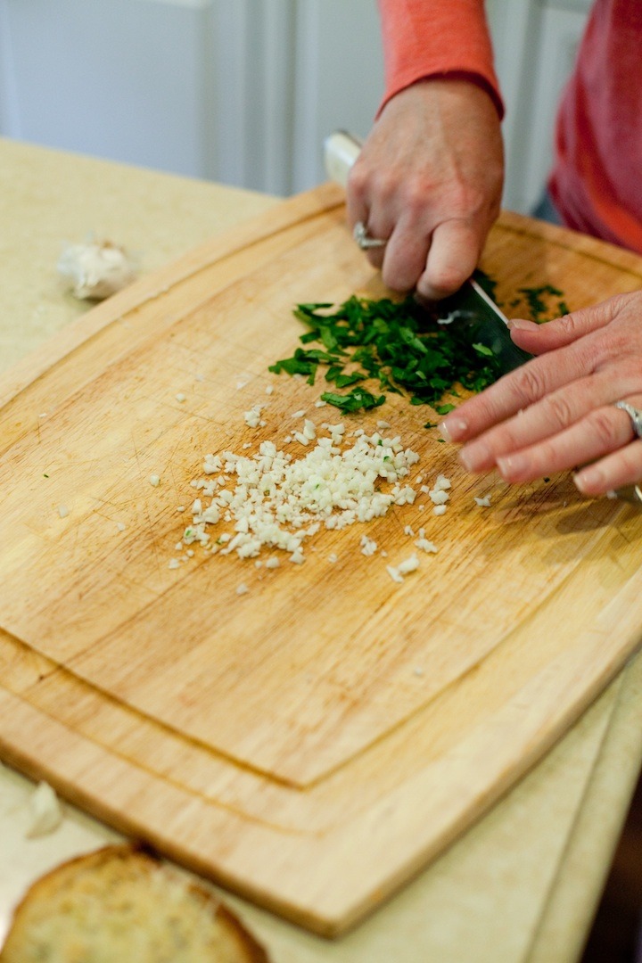 A woman holding a knife and chopping parsley and garlic to use as a  garnish for Chicken Piccata from The Organic Kitchen