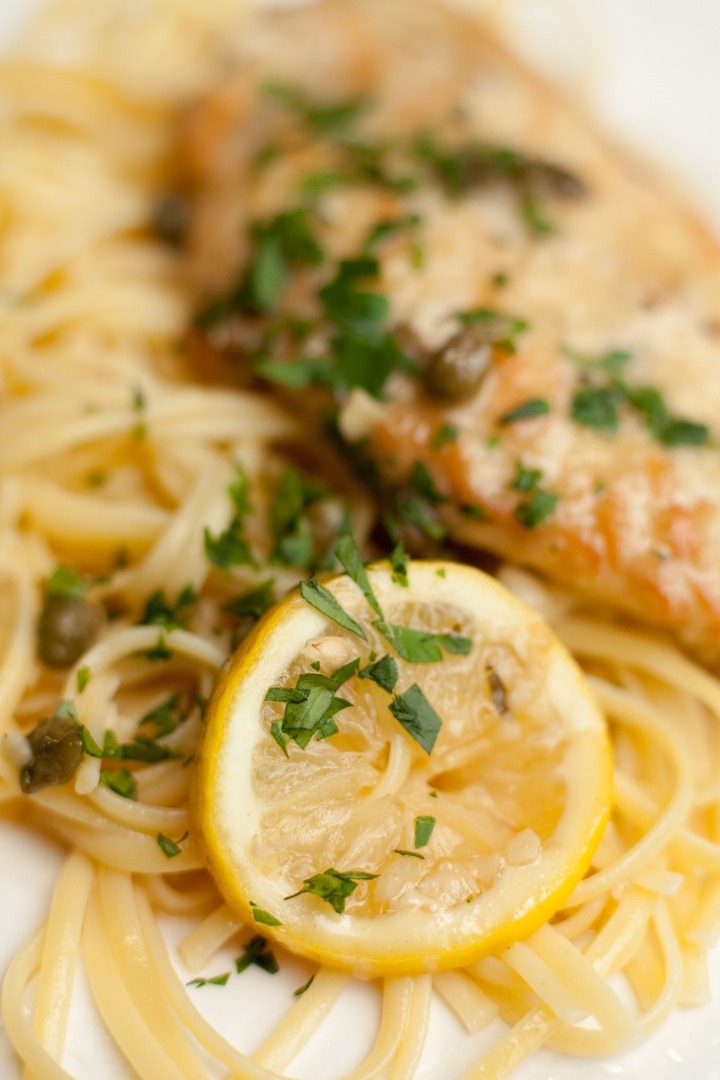 A close up of Chicken Piccata  with lemon slices on a white plate