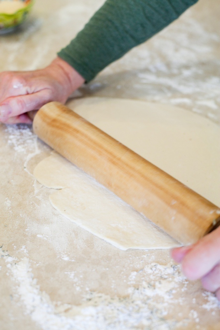 A woman's hands using a rolling pin to roll dough for Fresh Tomato and Basil Pesto Pizza