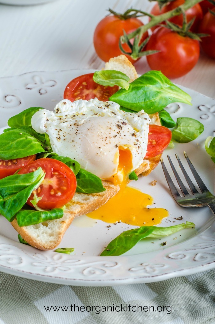 A white plate with Poached Eggs and Veggies on Toast with tomatoes in the background
