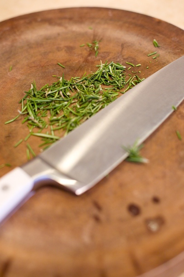A cutting board and knife with Chopped Rosemary used in the recipe for Greens Salad with Peaches 