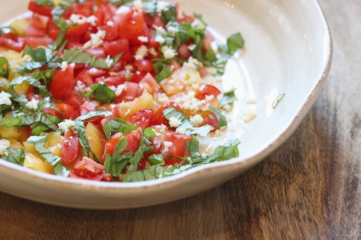 Chopped tomatoes, garlic, and basil in a large white bowl on wooden table. Heirloom Tomato Linguini from The Organic Kitchen