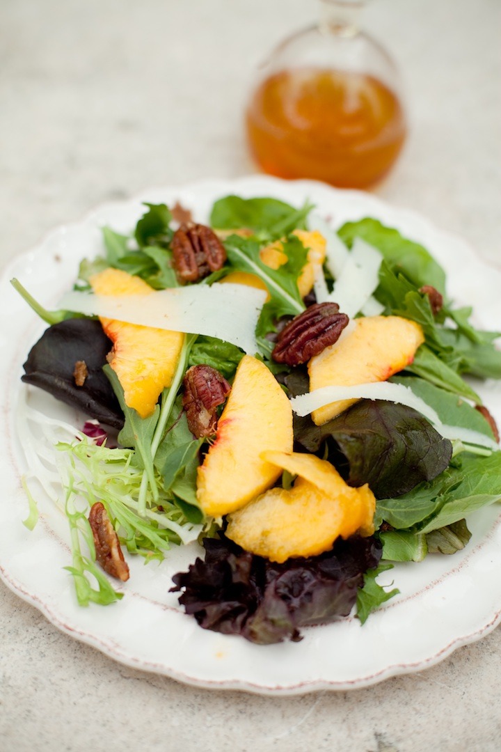 Greens with Peaches set on a white plate with a bottle of vinaigrette