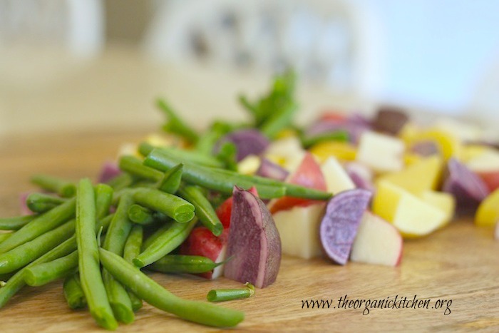 The ingredients for Tri-colored Potato Salad with Green Beans and Rustic Pesto on a cutting board: green beans, purple, white and rose potatoes