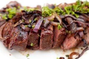 A close up photo of sliced tri-tip garnished with caramelized onions and chives