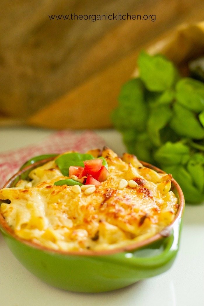 A green baking dish filled with 'baked penne rigate with a kick' on a white surface in front of fresh basil and wood cutting boards