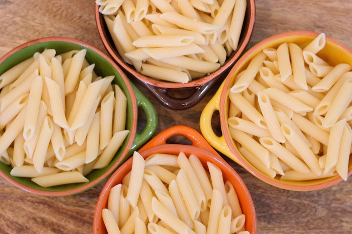Four colorful dishes filled with cooked penne rigate