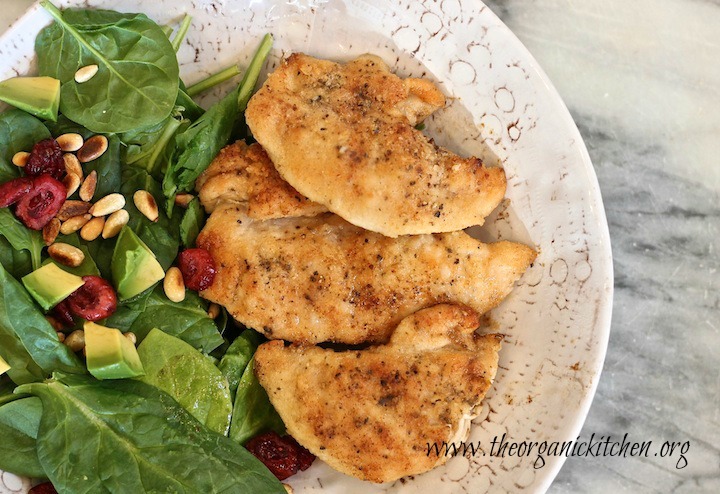 Three golden Easy Chicken Tenders in a white dish with spinach leaves